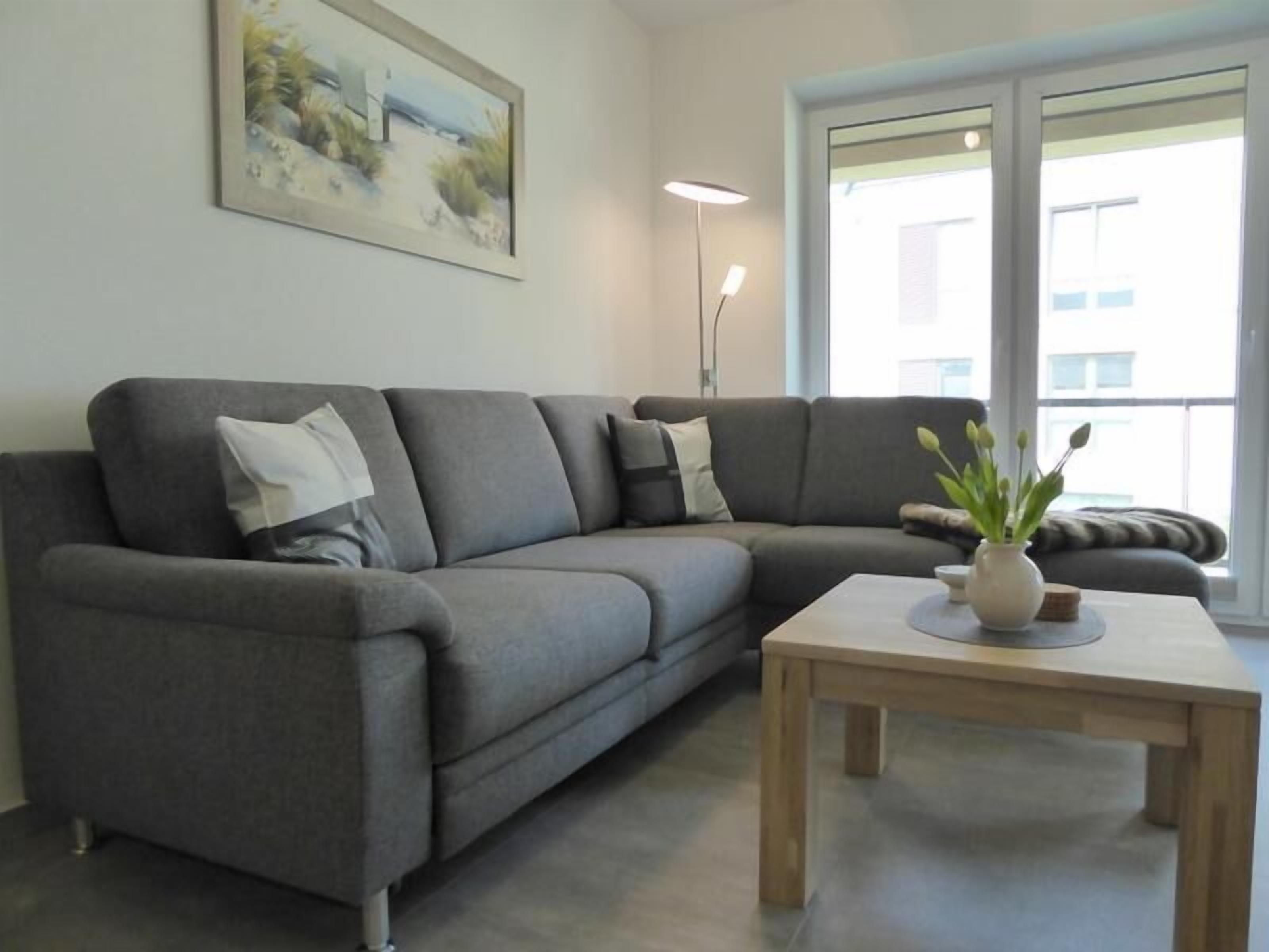Un salon moderne avec un canapé d’angle gris, une table basse en bois et un tableau accroché au mur.