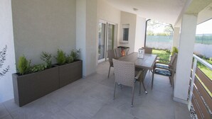 Un patio exterior con una mesa y sillas, una jardinera con plantas, y vistas al exterior.