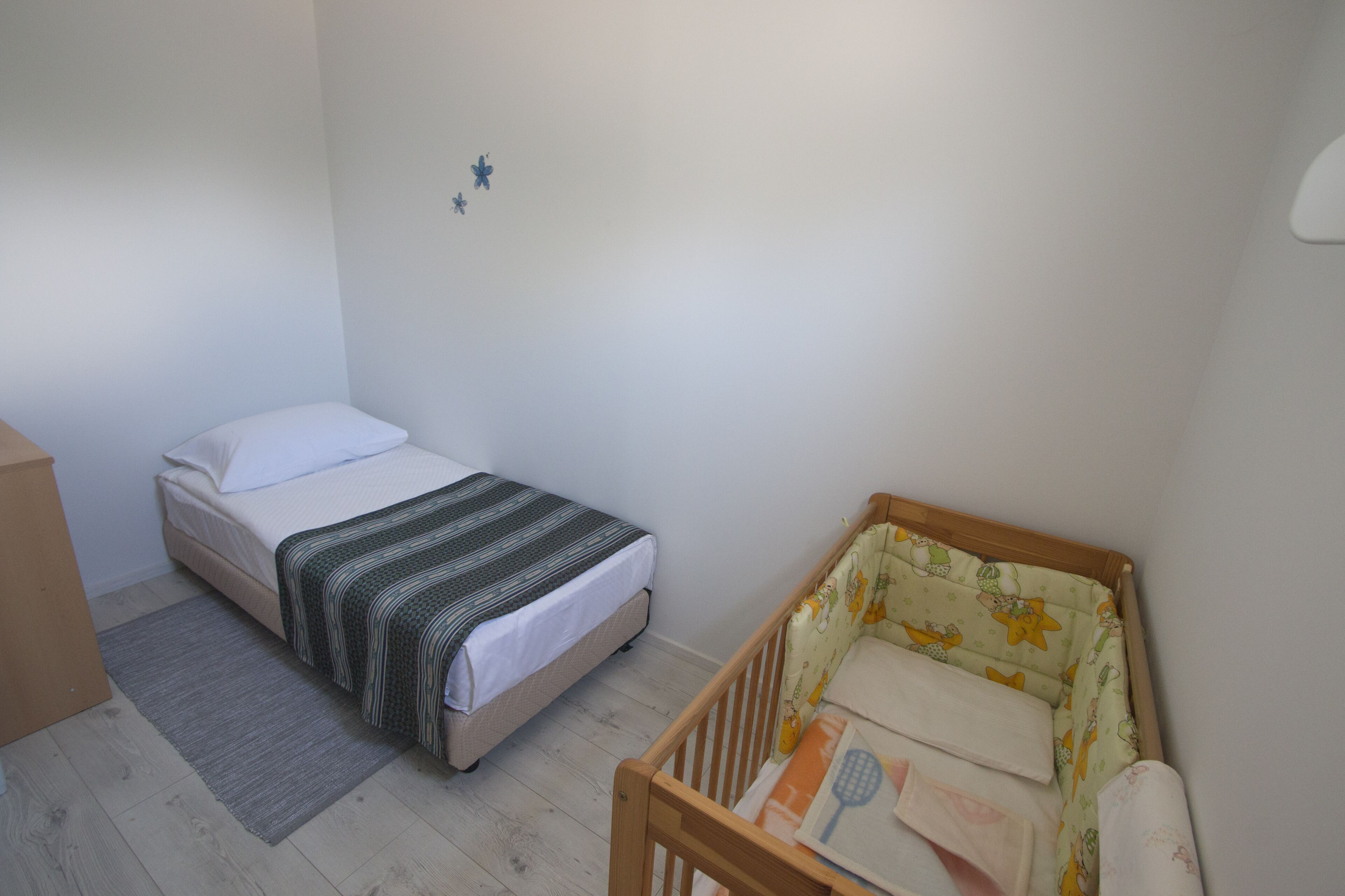 Una stanza piccola e pulita con un letto singolo, una culla e un comò di legno.