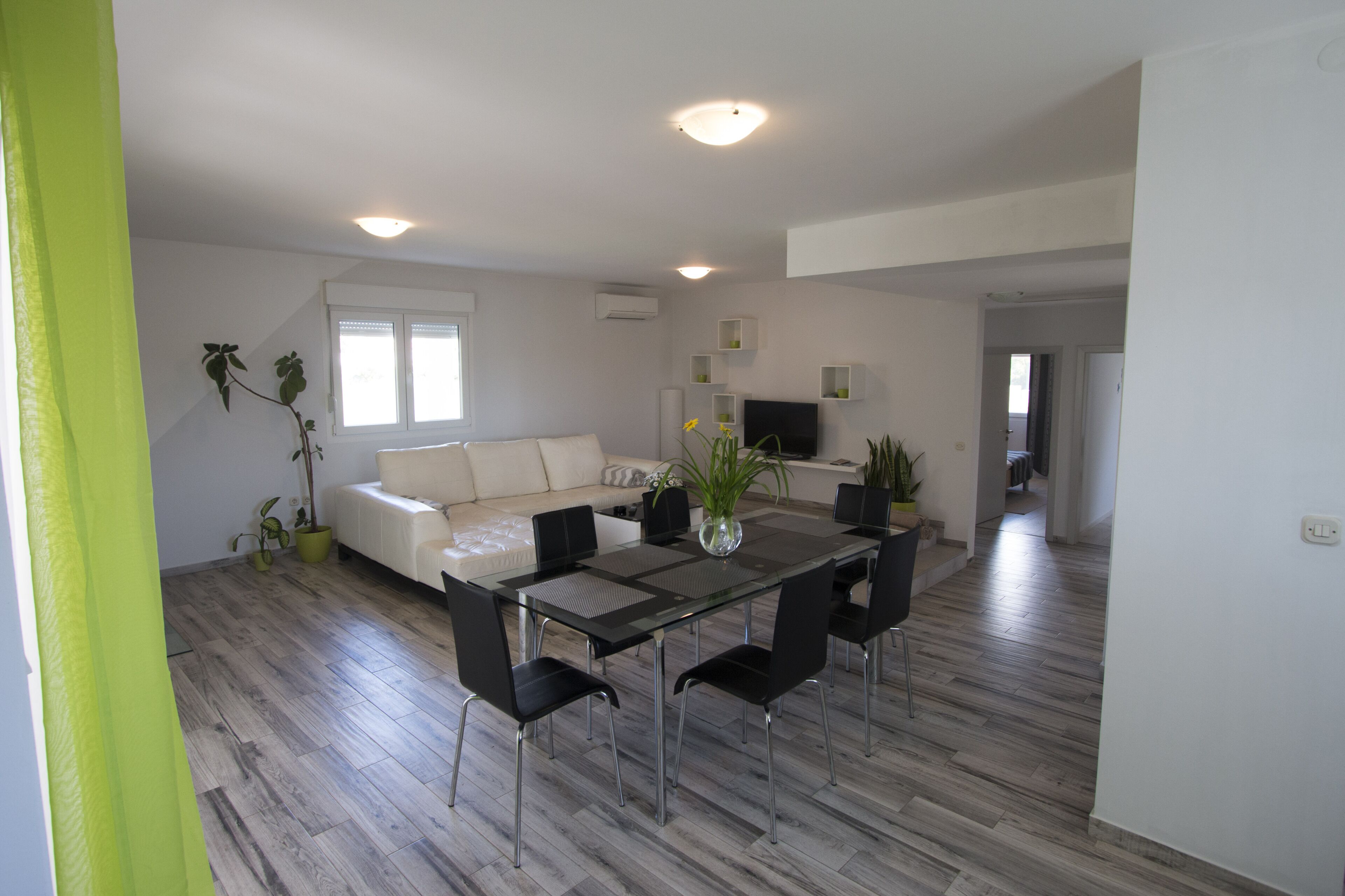 Un salon moderne avec une table à manger en verre, des chaises noires, un canapé blanc et un téléviseur.