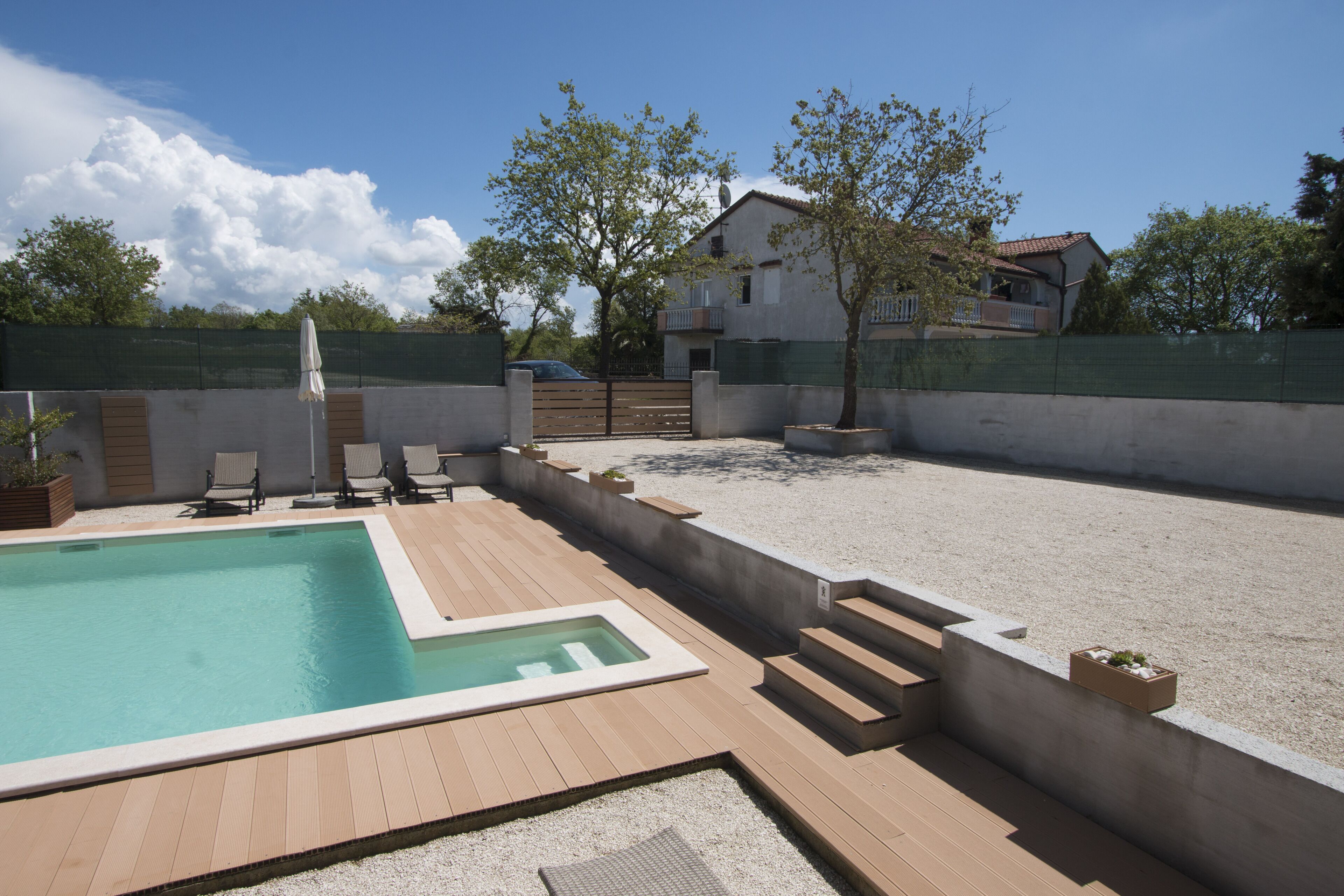 Una piscina amb un solàrium de fusta, un petit banyera hidromassatge i una zona tancada amb gandules.