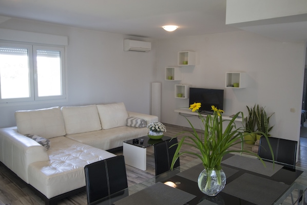 A modern living room with a white sofa, a glass coffee table, and a TV on a stand.