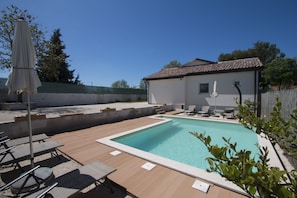 A swimming pool with lounge chairs and a covered umbrella, surrounded by a wooden deck and a white building with a tiled roof. - Cosy and lovely Villa Trosti with a pool (Svetvincenat)