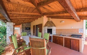An outdoor patio with a stone fireplace, wooden furniture, and a tiled backsplash. - Lovely Villa Ana (Svetvincenat)