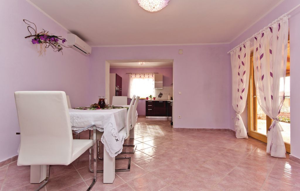 Uma área de refeições com mesa e cadeiras, uma cozinha ao fundo e uma vista pela janela com cortinas.