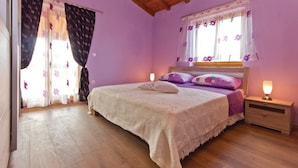 A bedroom with a wooden floor, a bed with a white blanket, purple pillows, and a nightstand with a lamp. - Lovely Villa Ana (Svetvincenat)
