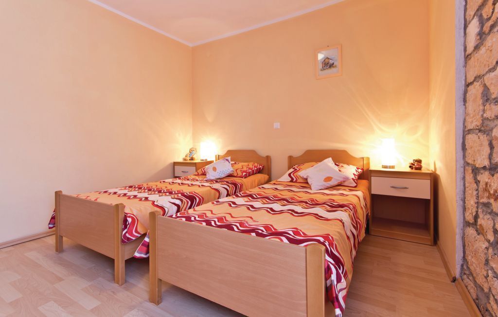 A bedroom with two wooden beds, each with a nightstand and a lamp. The room has a stone accent wall and a small picture on the wall.