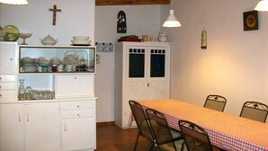 Een eetruimte met een tafel voor vier personen, omringd door metalen stoelen, een wit kastje met servies en een klok aan de muur.