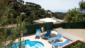 A pool area with lounge chairs and a view of a hillside with houses. - Private villa with fantastic sea view! (Lloret de Mar)
