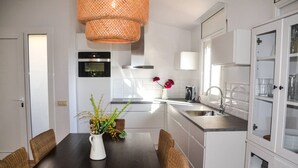 A modern kitchen with a dining table, wicker chairs, a white pitcher with flowers, and a hanging light fixture. - Private villa with fantastic sea view! (Lloret de Mar)