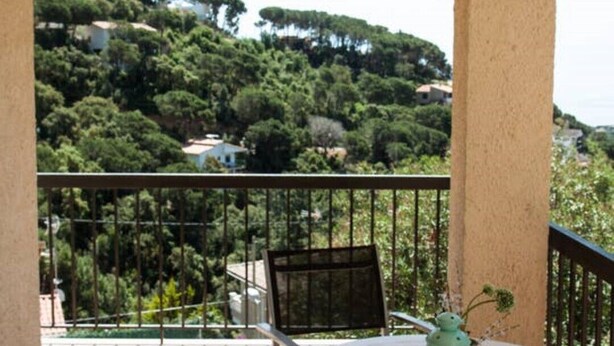 A balcony with a round table and chairs, overlooking a hillside with trees and buildings. - Private villa with fantastic sea view! (Lloret de Mar)