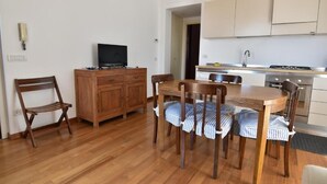 Un espace de vie compact comprenant un coin repas, une kitchenette et un téléviseur posé sur un meuble en bois.