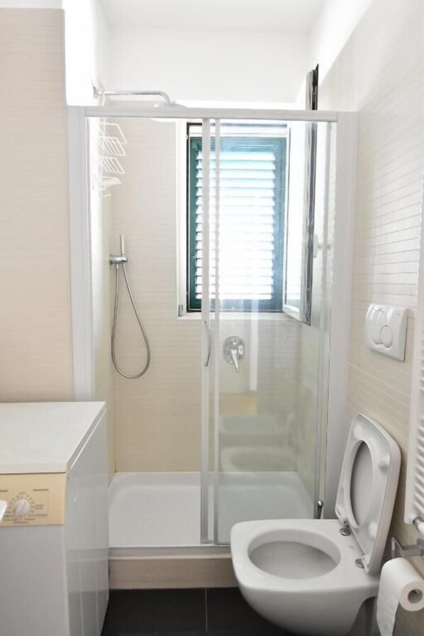 A modern bathroom with a glass-enclosed shower, a toilet, and a window providing natural light.