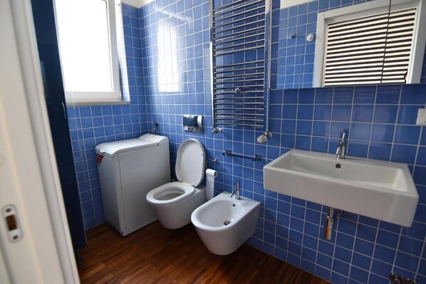 A bathroom with blue tiles, a white sink, a toilet, and a bidet.