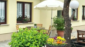 An outdoor seating area with a table, chairs, a potted plant, and a white umbrella.