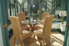 A round glass table with wicker chairs, a small potted plant, and a lamp on a green wall.