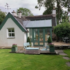 A house with a green roof, a conservatory with glass doors, and a patio with outdoor furniture.