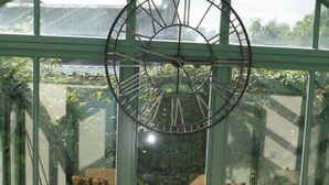 A round glass table with woven chairs in a greenhouse.