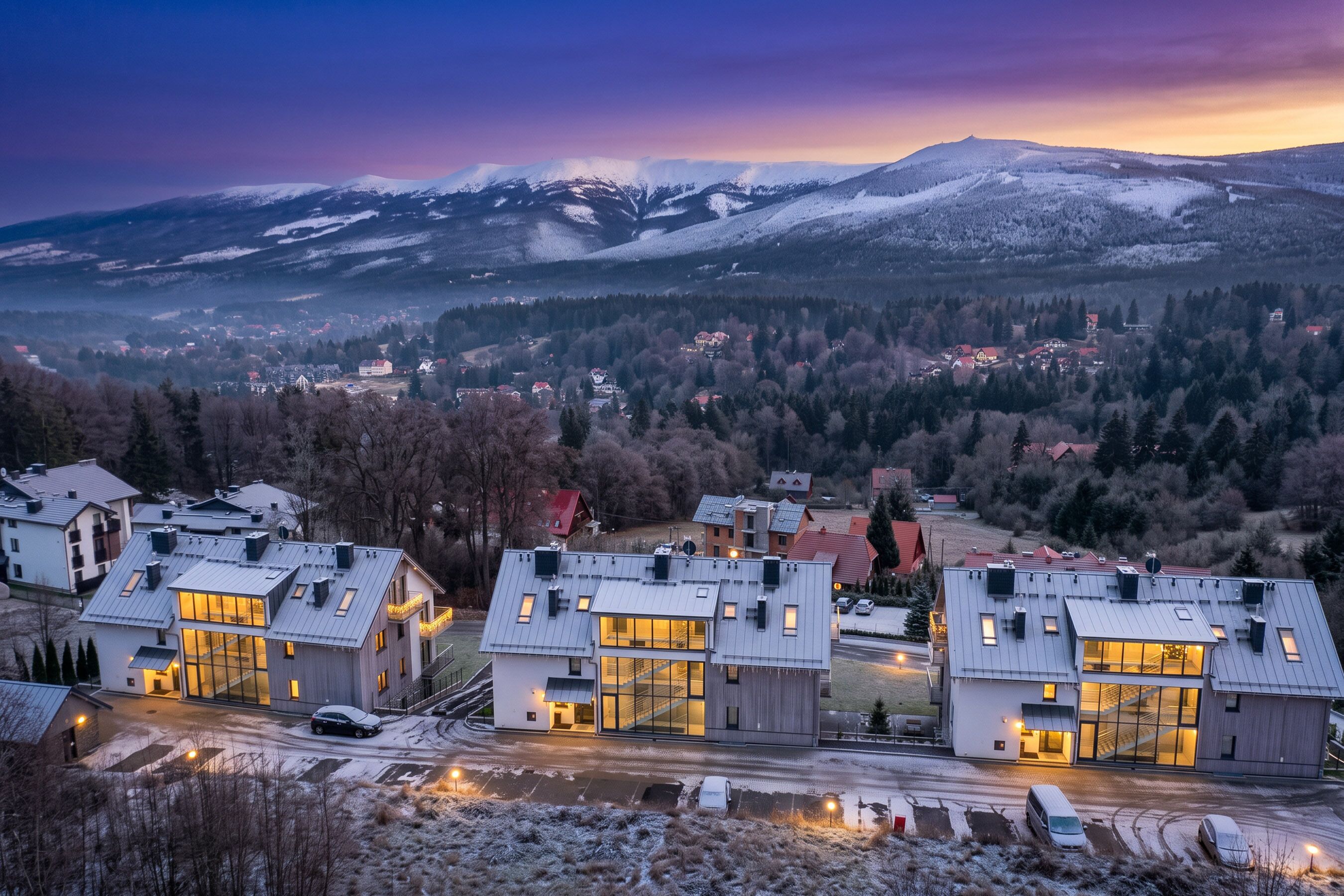 A modern residential area with contemporary houses, a snowy landscape, and a mountain range in the background.