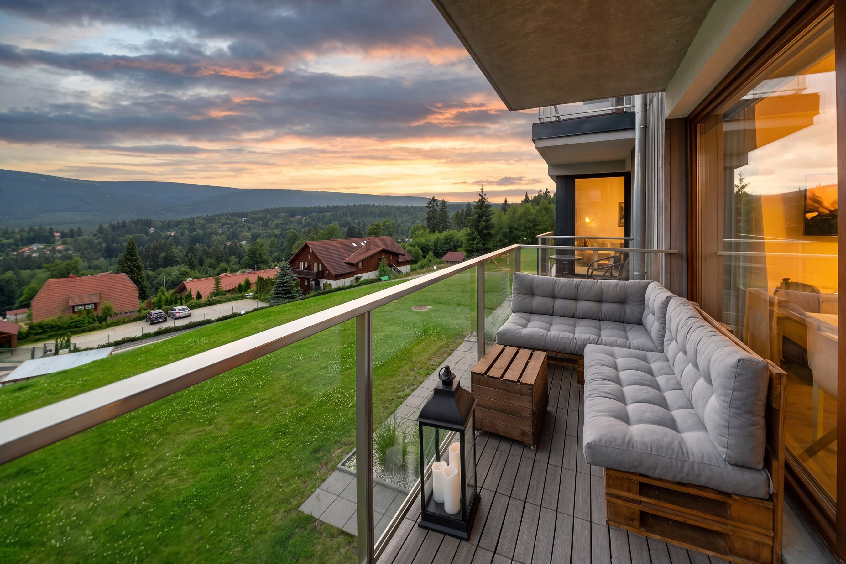 A balcony with a sofa and a table, overlooking a green landscape and houses.