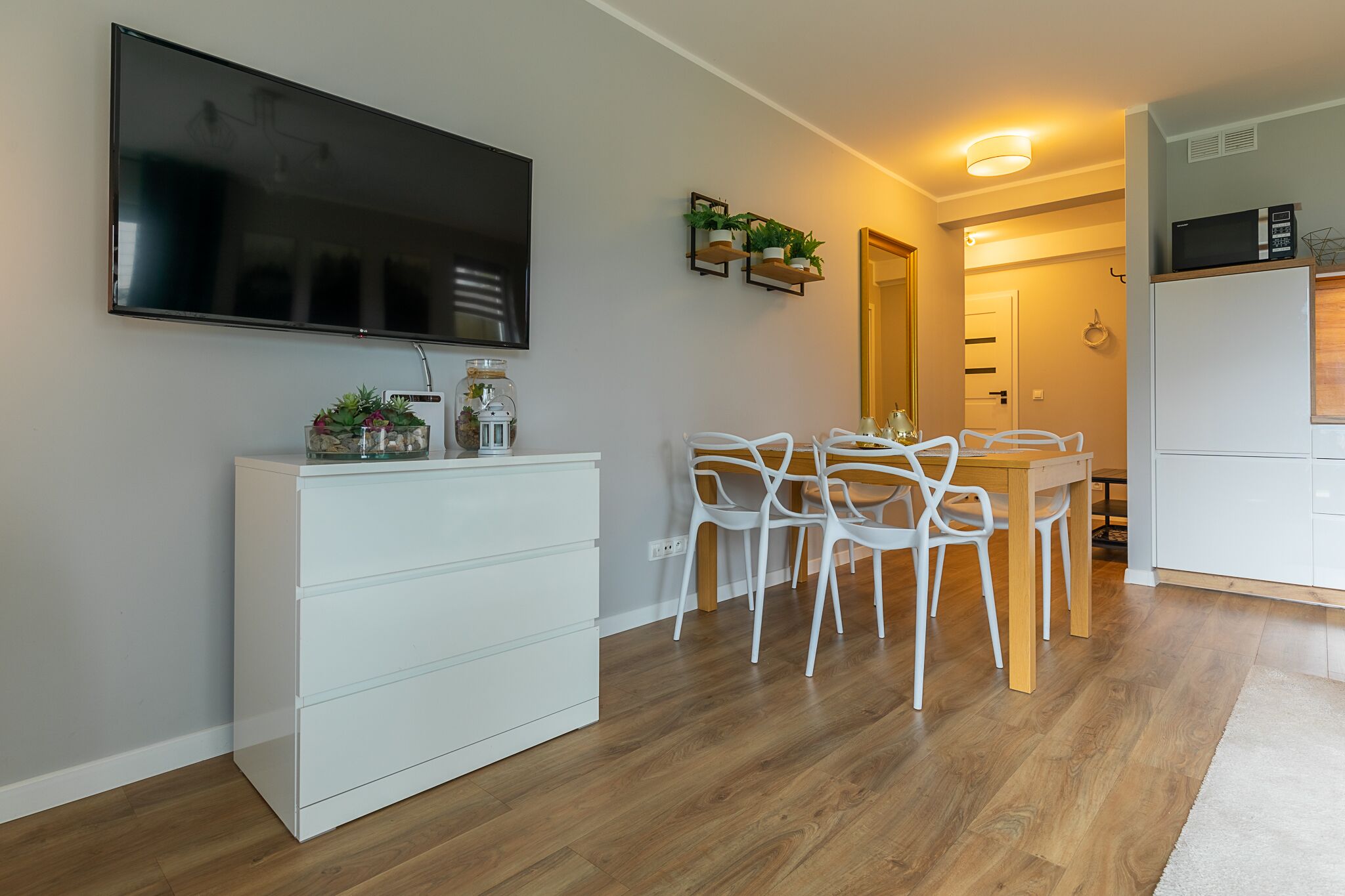 Una cocina moderna con armarios blancos, un microondas y un comedor con sillas blancas y una mesa de madera.