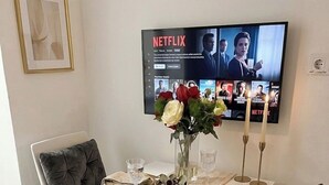 A dining area with a white table set for four, a vase with flowers, a television displaying Netflix content, and a framed picture on the wall. - Tortosa Stari Grad (Split)
