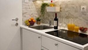 A modern kitchen with white cabinets, a black countertop, a sink, a wine bottle, and a fruit bowl. - Tortosa Stari Grad (Split)