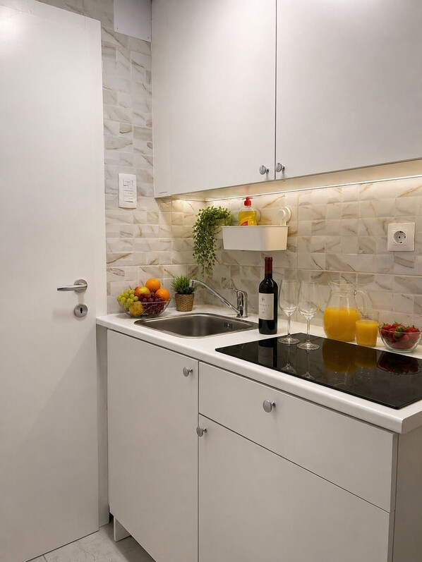 A modern kitchen with white cabinets, a black countertop, a sink, a wine bottle, and a fruit bowl.