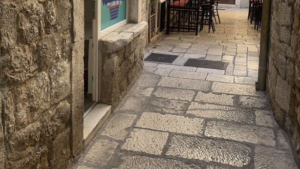 A narrow street with stone pavement, a laundry service sign, and outdoor seating. - Tortosa Stari Grad (Split)