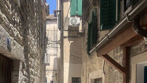 A narrow stone-paved alleyway between buildings with stone walls, a door, and a window with green shutters. - Tortosa Stari Grad (Split)
