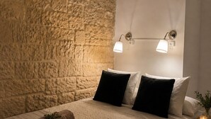 A bedroom with a stone wall, a bed with rolled towels, two wall-mounted lights, and an air conditioning unit. - Tortosa Stari Grad (Split)