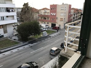 A street view with buildings, parked cars, and a pedestrian. - Tortosa Blue (Split)
