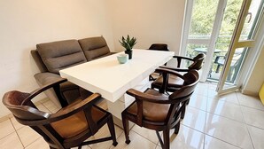 Een eetgedeelte met een witte tafel, bruine stoelen, een potplant en uitzicht door een glazen deur.
