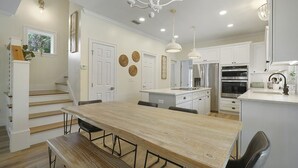 A modern kitchen with white cabinetry, a wooden dining table, and a staircase leading to an upper level. - Beach Baby - Secluded Home with Private Pool Area & Deck (Santa Rosa Beach)