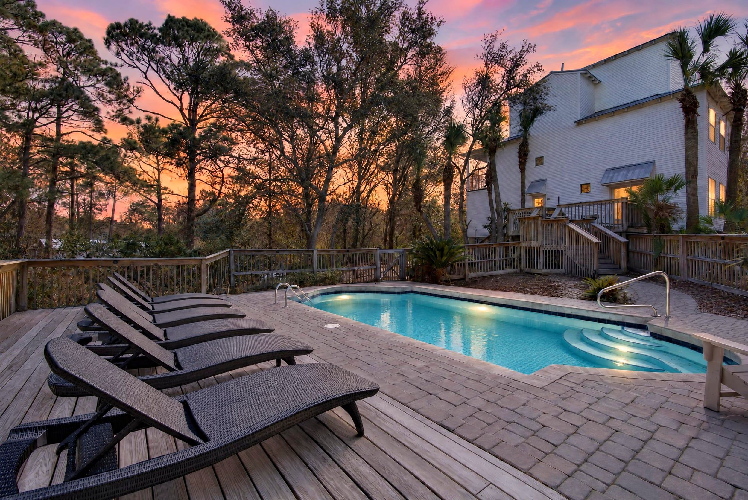 A swimming pool with lounge chairs and a wooden deck, surrounded by trees and a building.