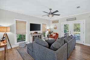 A living room with a sectional sofa, a flat-screen TV, and a ceiling fan. - Beach Baby - Secluded Home with Private Pool Area & Deck (Santa Rosa Beach)