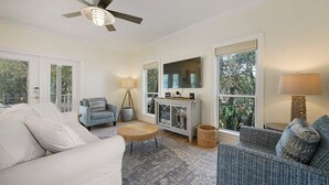 A spacious living room with a white sofa, blue armchairs, a round coffee table, and a television on a cabinet. - Beach Baby - Secluded Home with Private Pool Area & Deck (Santa Rosa Beach)
