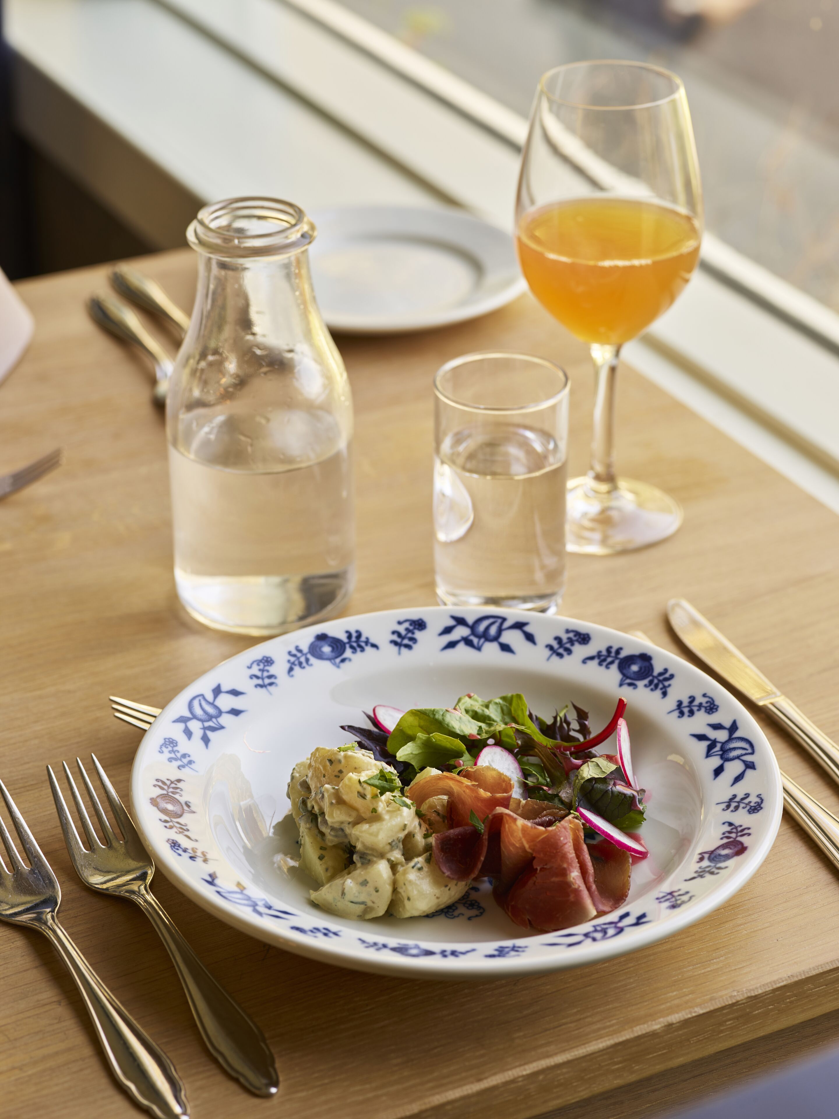 A plate of food with a salad, a small bowl of soup, and a glass of orange juice on a wooden table.