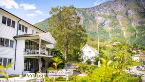 A two-story building with a balcony, a garden with outdoor seating, and a mountain backdrop. - Heimly (Aurland)