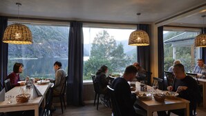 A dining area with tables and chairs, large windows with a view of a mountainous landscape, and hanging wicker lamps. - Heimly (Aurland)