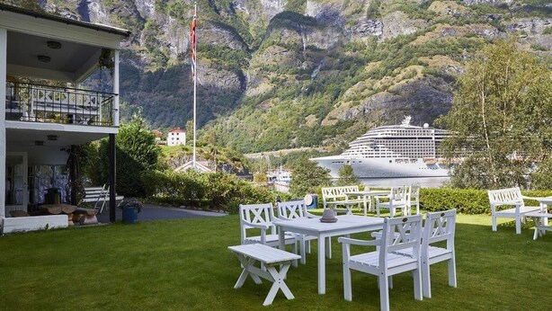 A hotel with outdoor seating and a view of a cruise ship in the background. - Heimly (Aurland)