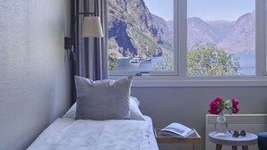 A bedroom with a bed, a nightstand, a table with a vase of flowers, and a view of a mountainous landscape through large windows. - Heimly (Aurland)