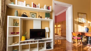 A living room with a TV, shelves with books and decorative items, a dining area with a table and chairs, and a patterned rug. - Kaptol Residence (Zagreb)