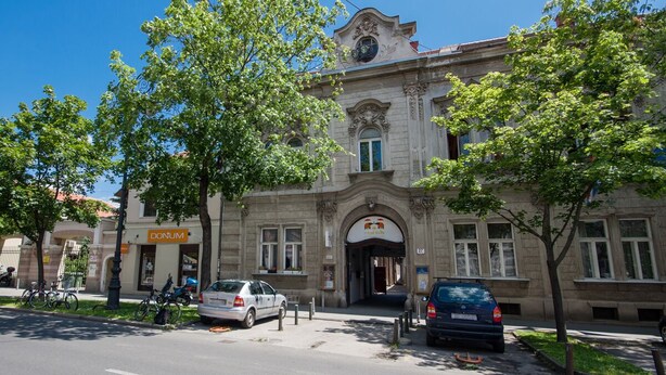 A historic building with a central entrance, a 'DONUM' sign, and parked cars on the street. - Kaptol Residence (Zagreb)
