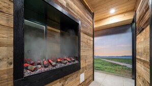 A modern interior with a large fireplace, wooden paneling, and a view of a landscape through a glass wall. - RentPlanet - Apartament Goszczyńskiego (Zakopane)