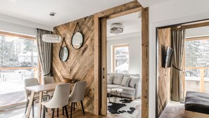 A modern living space with a wooden accent wall, a dining area with chairs, a sofa, and a TV mounted on the wall. - RentPlanet - Apartament Goszczyńskiego (Zakopane)
