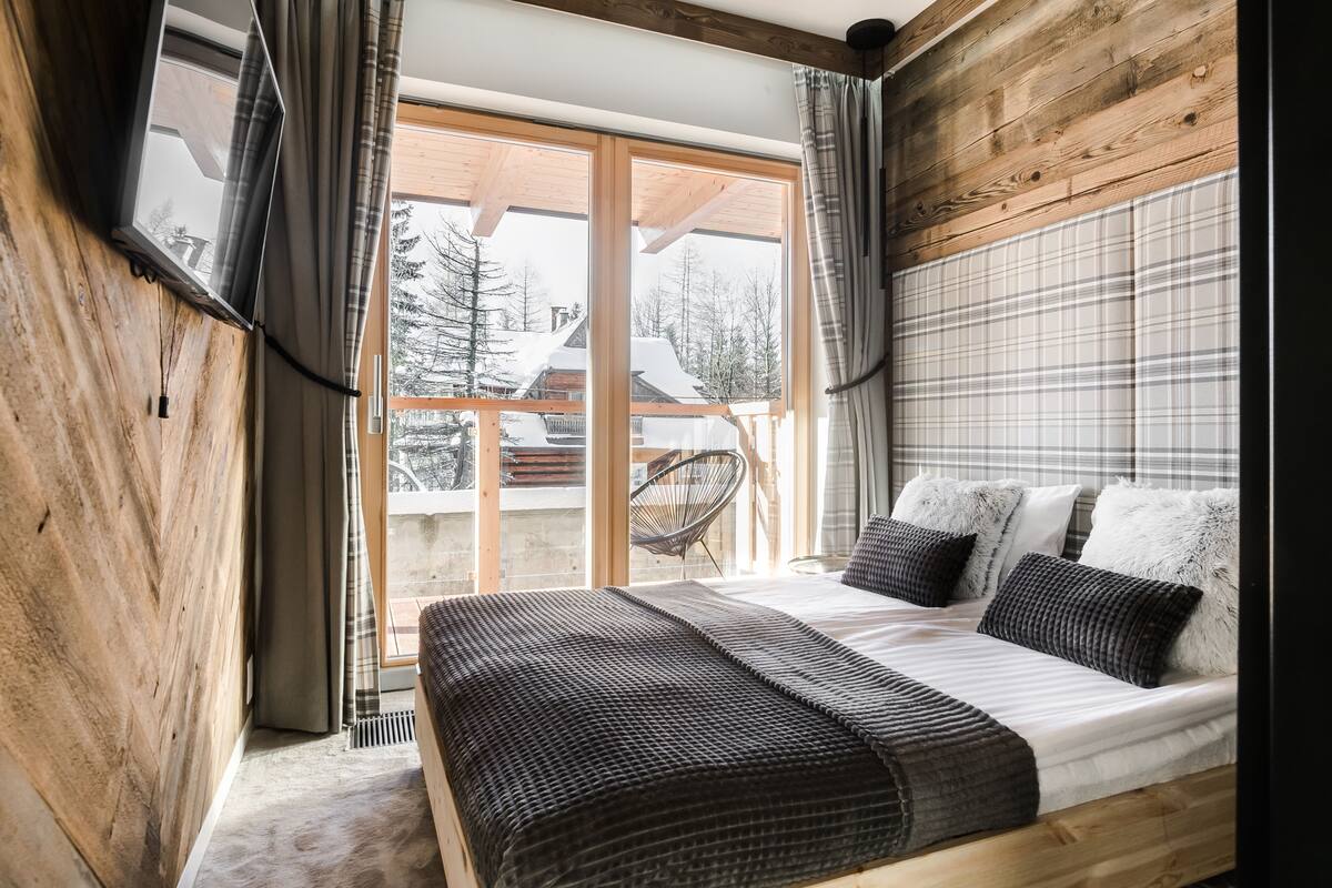 A bedroom with a large bed, wooden walls, and a view of the outside.