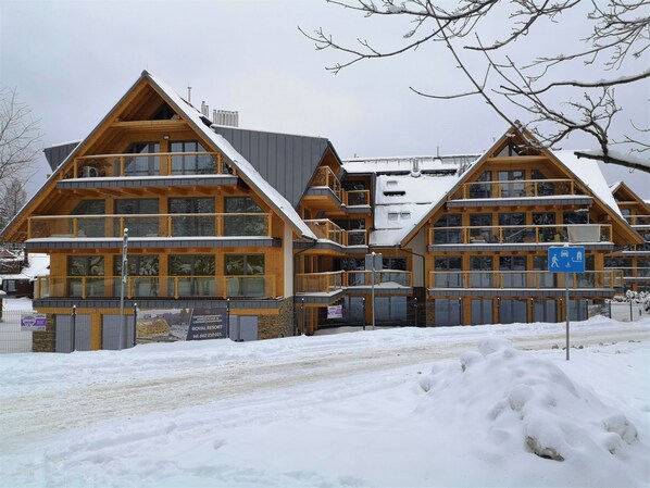 A multi-story wooden building with balconies, a sign indicating it is a hotel, and a snowy landscape in the foreground.