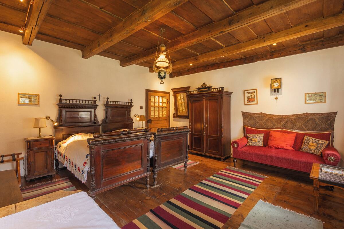 Une pièce meublée de meubles en bois, avec un lit, un canapé rouge et un lustre.