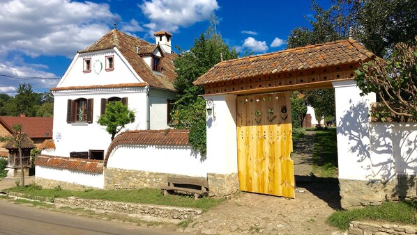 A traditional white building with a tiled roof, a wooden gate, and a stone wall. - Count Kalnoky's Transylvanian Guesthouse (Baraolt)